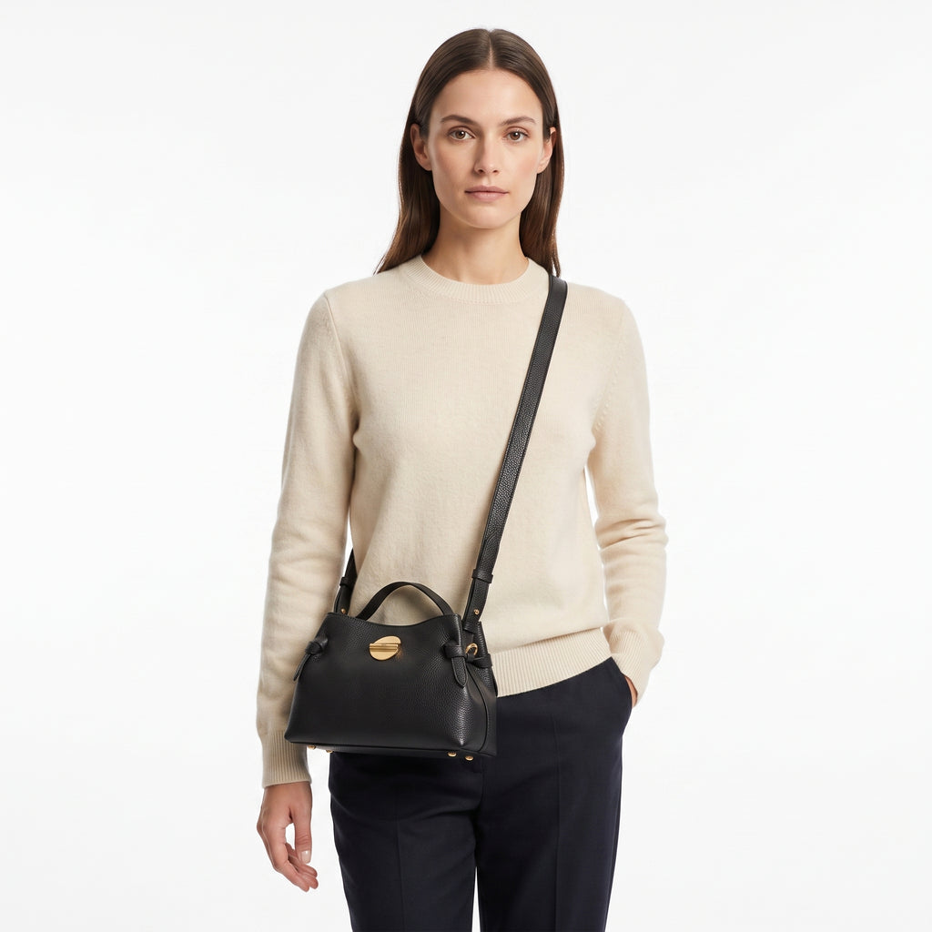 Woman wearing a beige sweater and carrying a black handbag on a white background