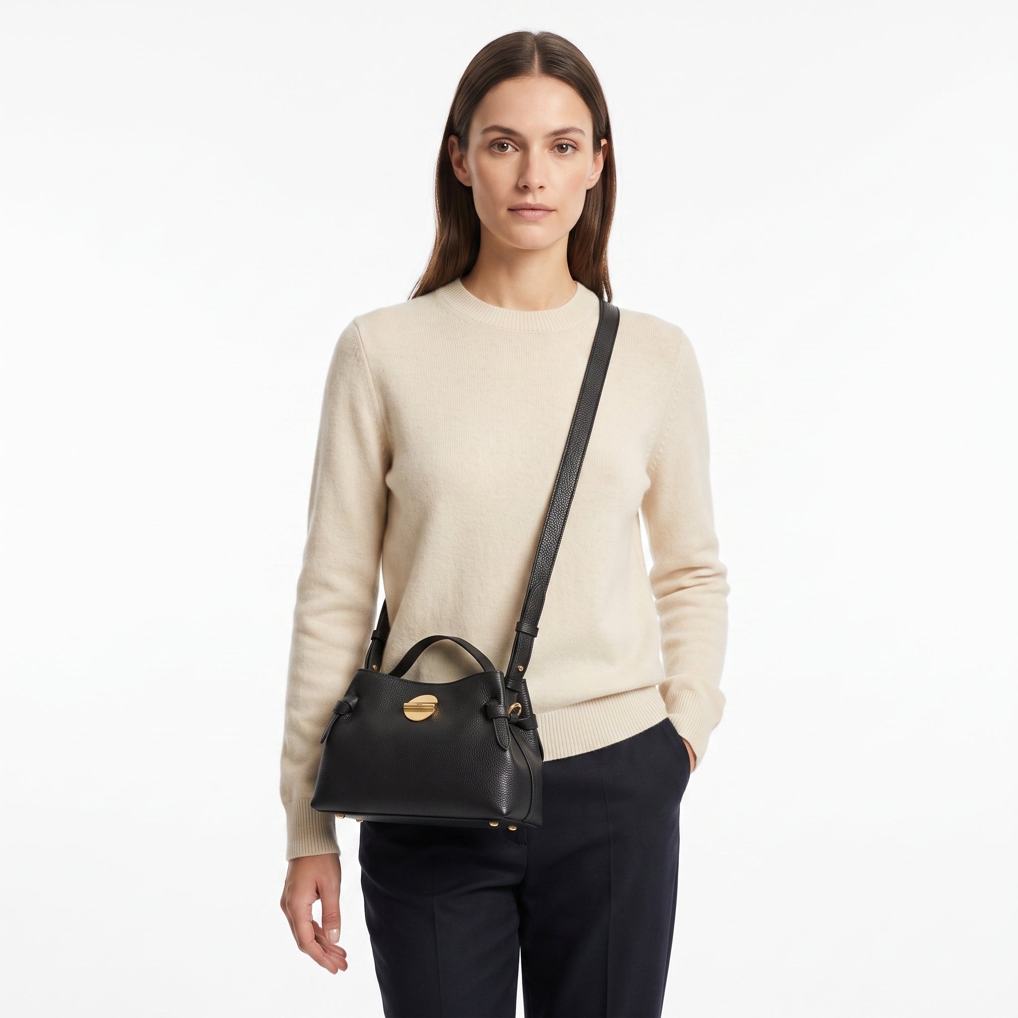 Woman wearing a beige sweater and carrying a black handbag on a white background